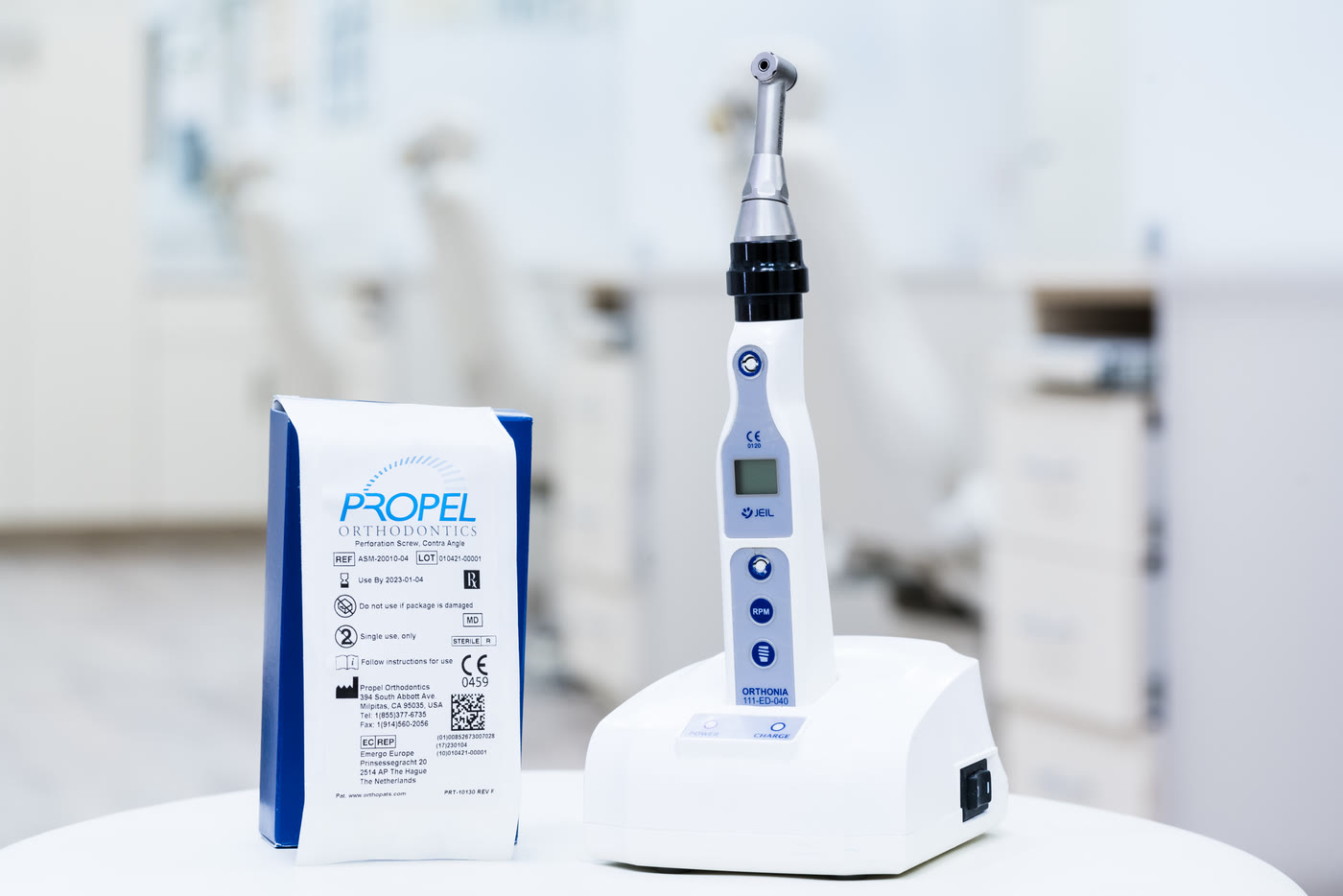 The handpiece used for micro-osteoperforations on its stand beside its sterile packaging